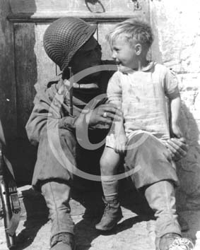 TREVIERES(14710) Seconde guerre mondiale Un soldat amricain tient dans ses bras, assis par terre, un jeune enfant de Trvires.